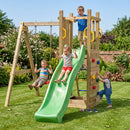 A large wooden outdoor playground set with a green slide, two hanging swings, and a climbing wall, shown in a grassy backyard with three children playing under a blue sky.