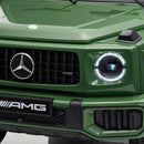 Close-up of the front end of a green Mercedes-Benz AMG vehicle, showing the Mercedes star emblem, AMG badge, round headlight with illuminated ring, and front grille.