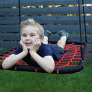 Child on a red and black rope swing in a garden setting