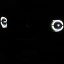 A close-up of a car front grille in complete darkness, showing two illuminated LED headlights with circular ring designs and a faint Mercedes-Benz star logo in the center.